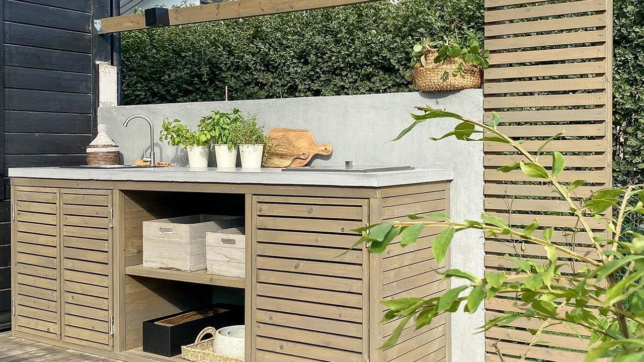 Utekjøkken med skapdører, benkeplate i betong og levegg med spiler.