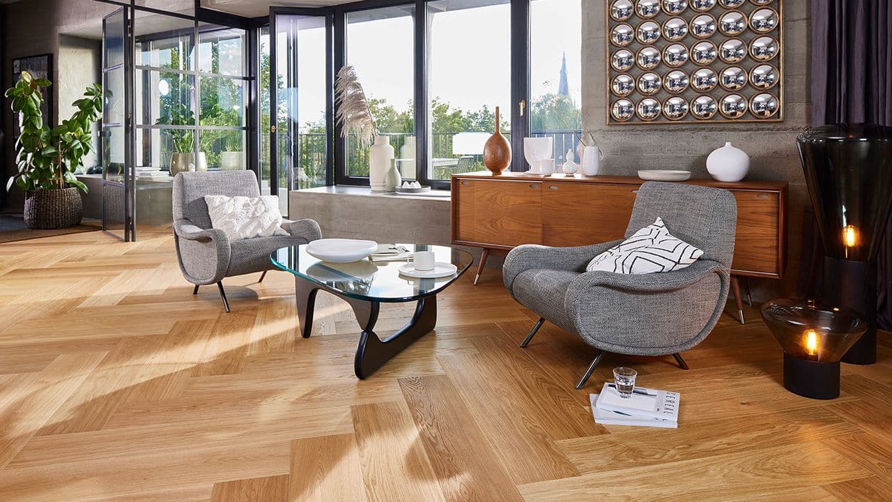 Stue med fiskebeinsparkett og moderne møbler i treverk og grått.