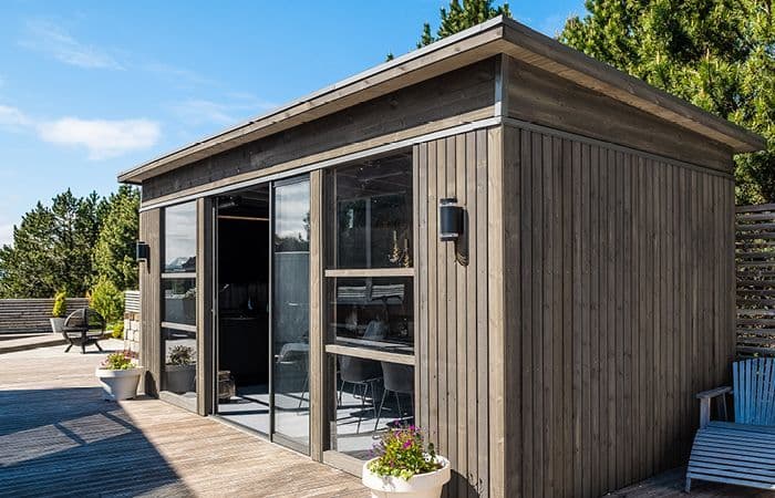 Hagestue byggesett med vinduer og skyvedører på terrasse.