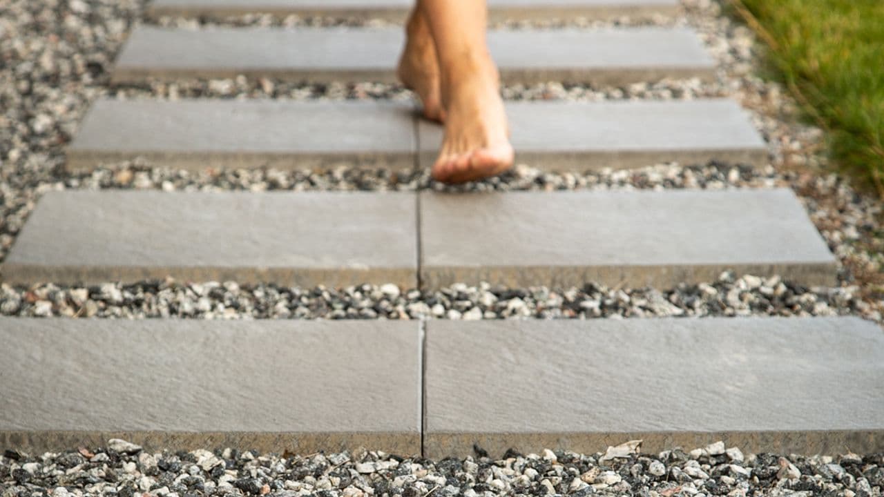 Barbeint kvinne går på en hagesti med steinheller og pyntestein langs plenen.