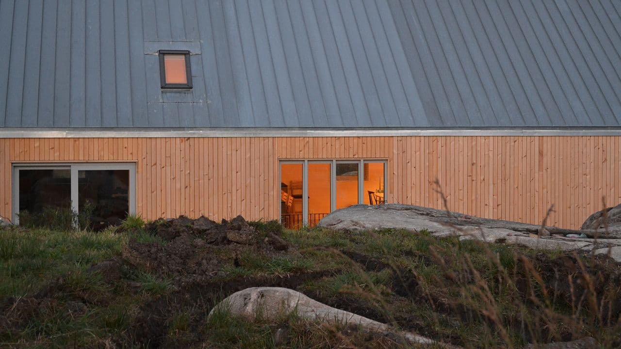 Stående kledning i malmfuru på hus med grått tak.