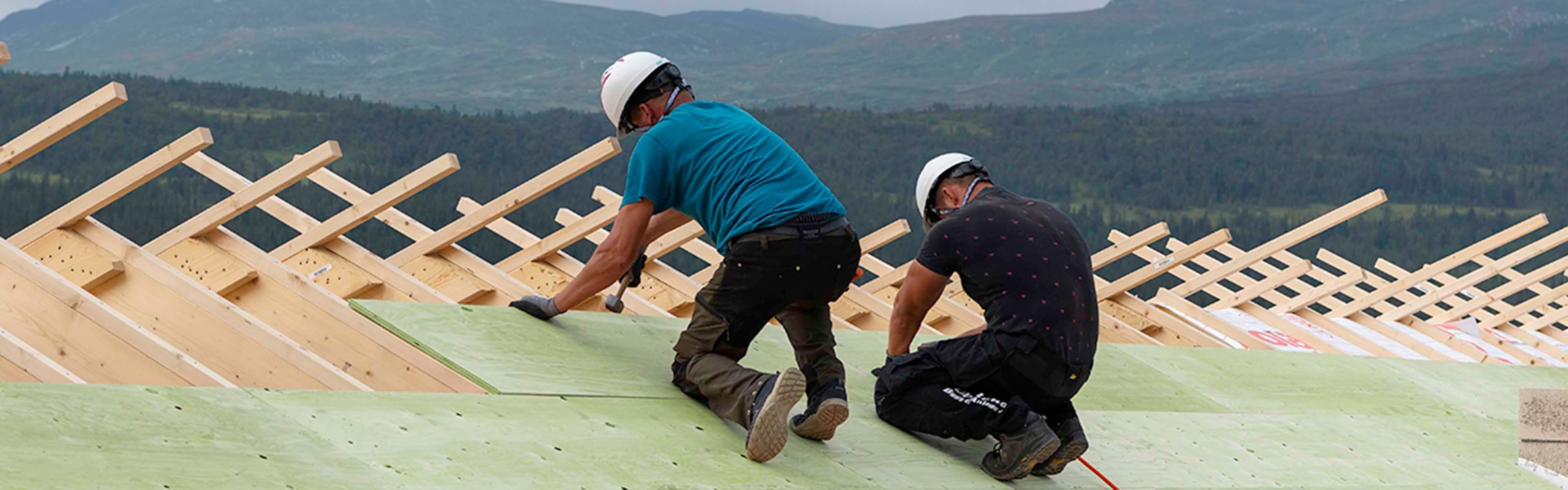 To håndverkere på tak som legger undertak av konstruksjonsplater av kryssfiner.