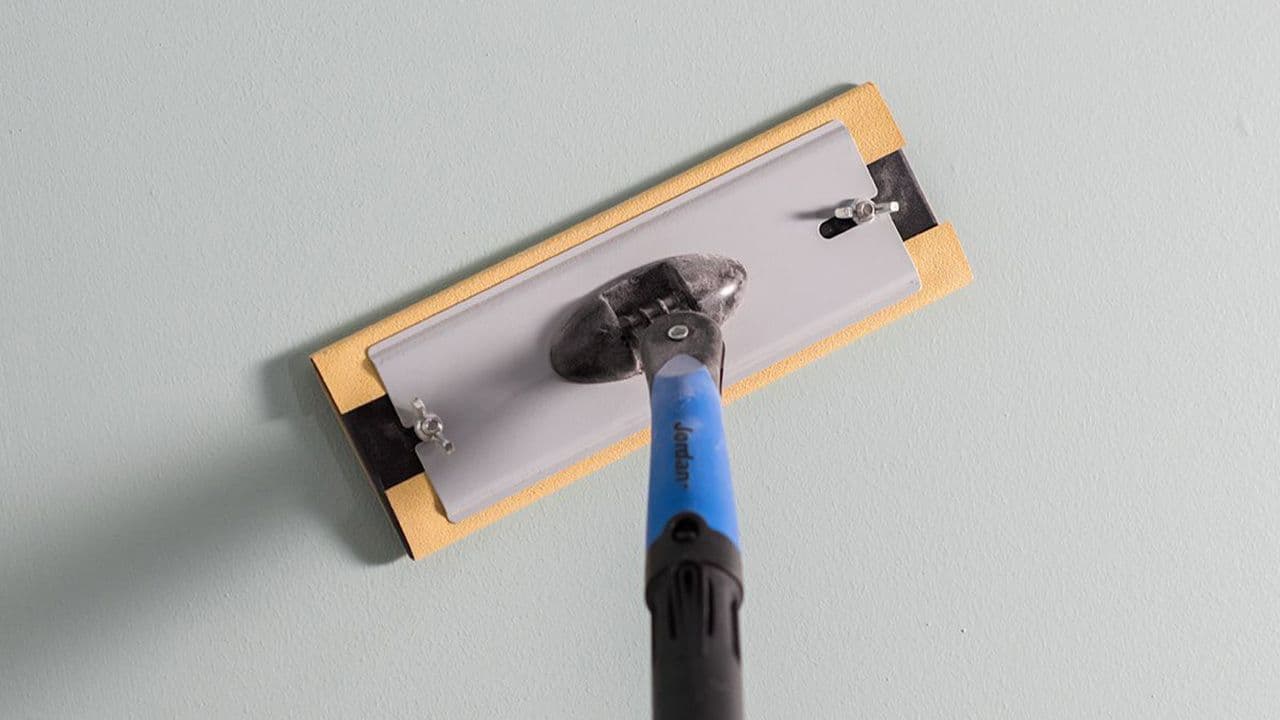 Slipebrett med forlengerskaft som sliper en helsparklet vegg.