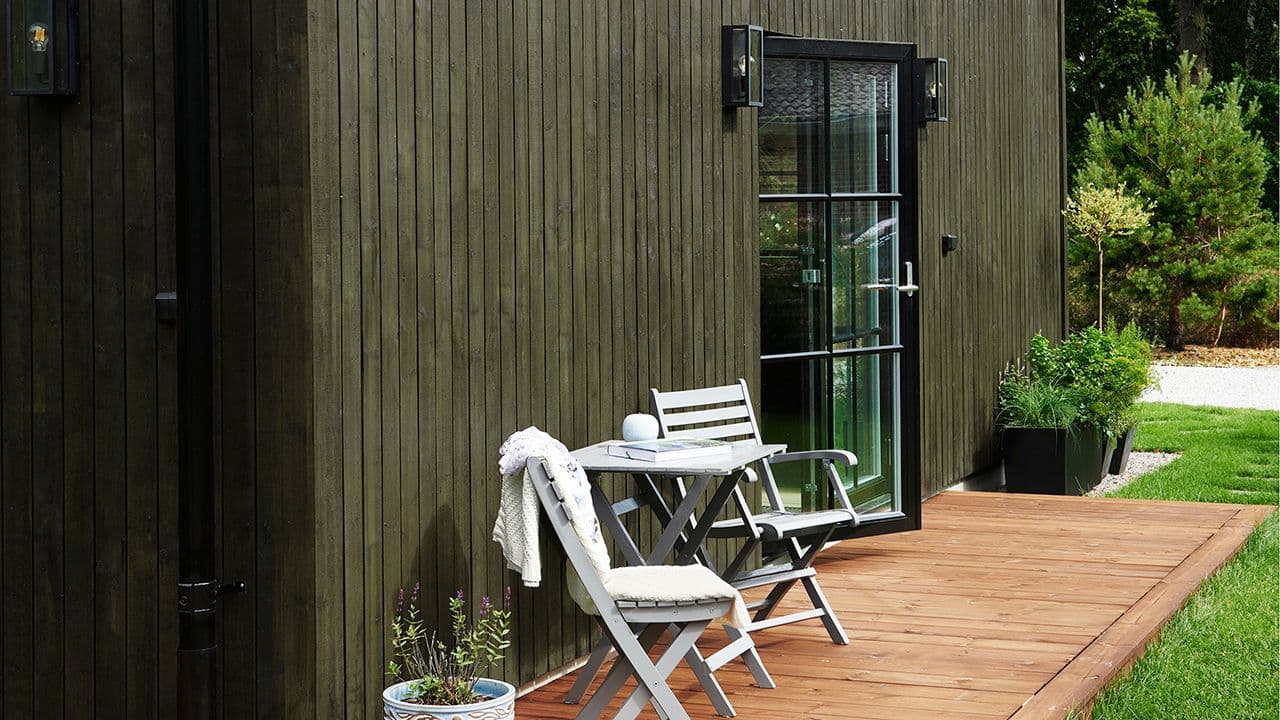 Hus med sort matt balkong dør og grønn beis som husfarge.