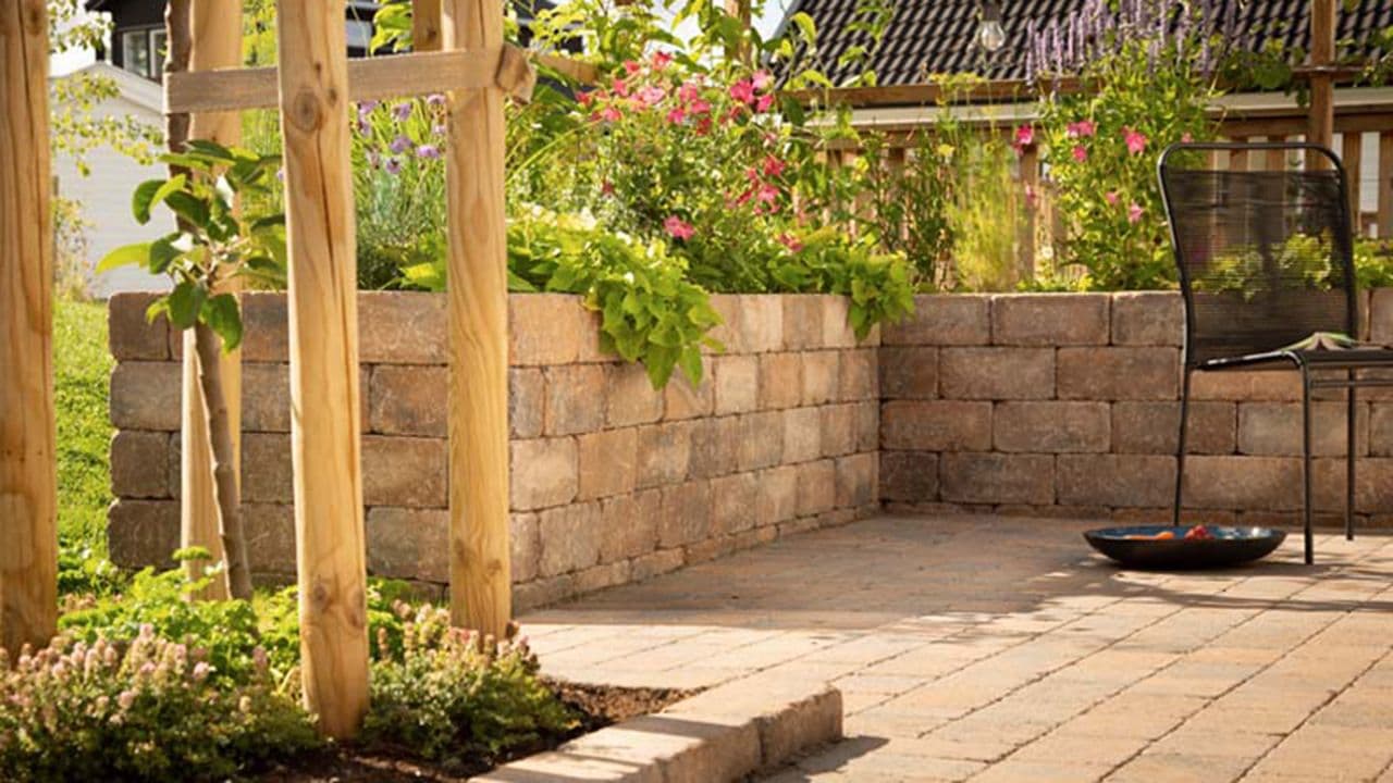 Blomsterbed med mur av belegningsstein og frodig hage.