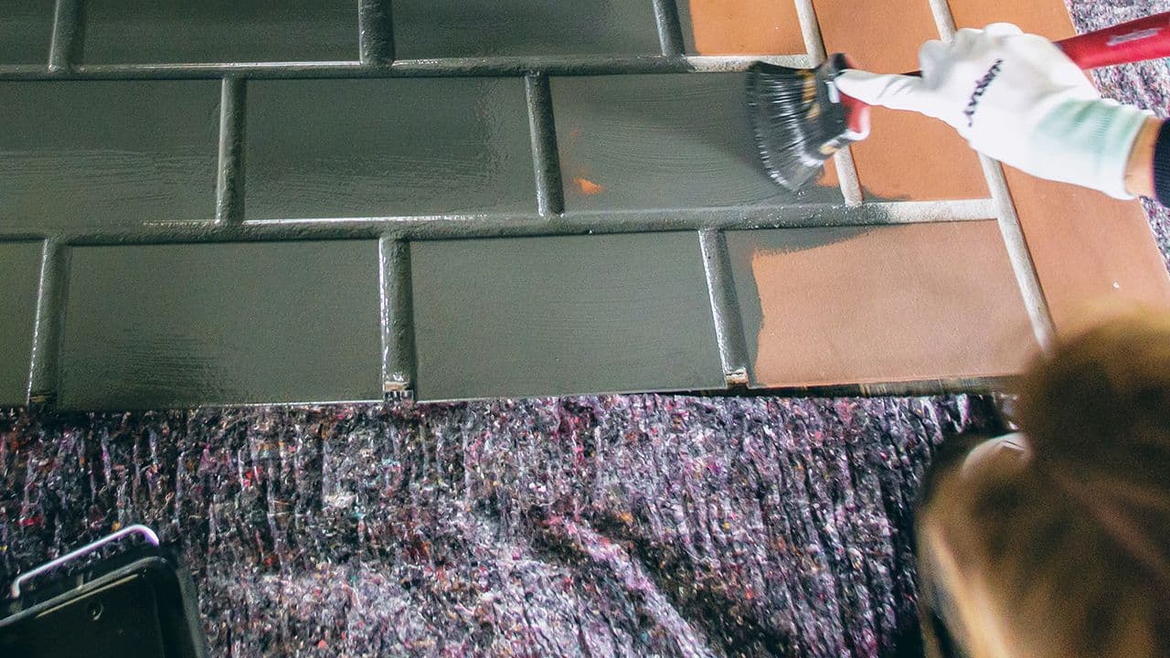 Kvinne som holder på å male fliser gulv med pensel.