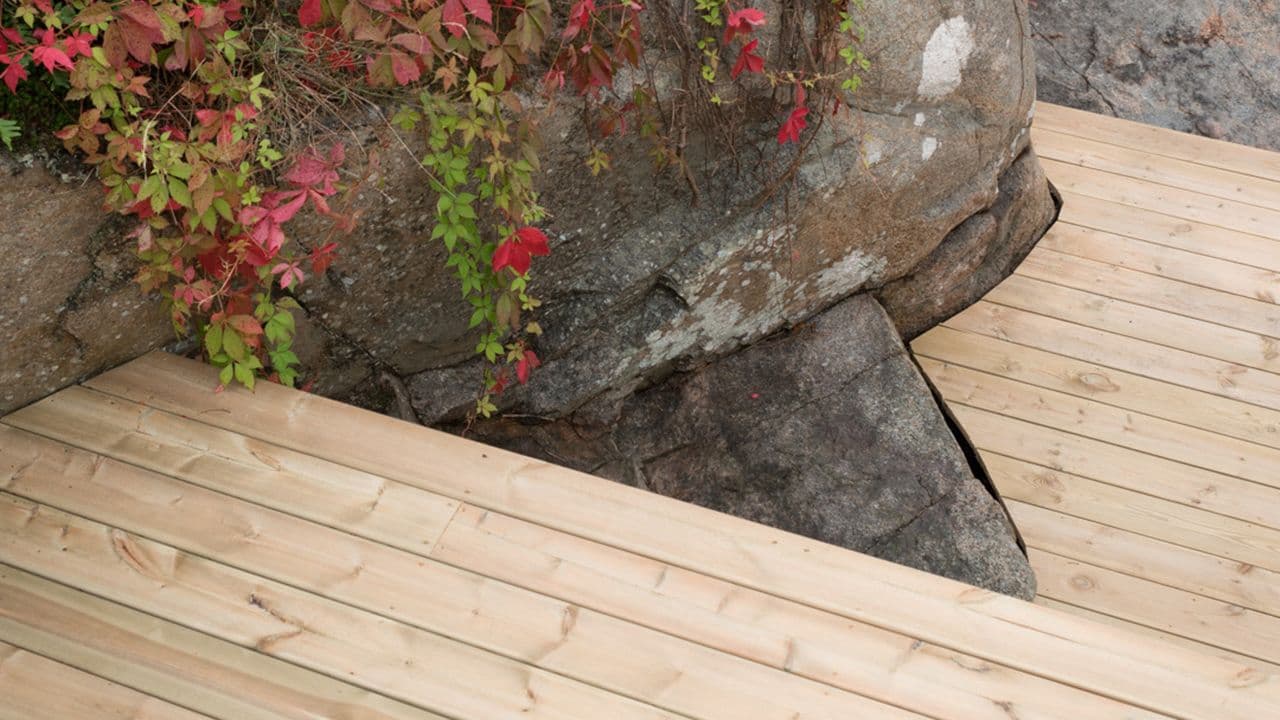 Terrassetrapp av trykkimpregnerte terrassebord inntil stein.