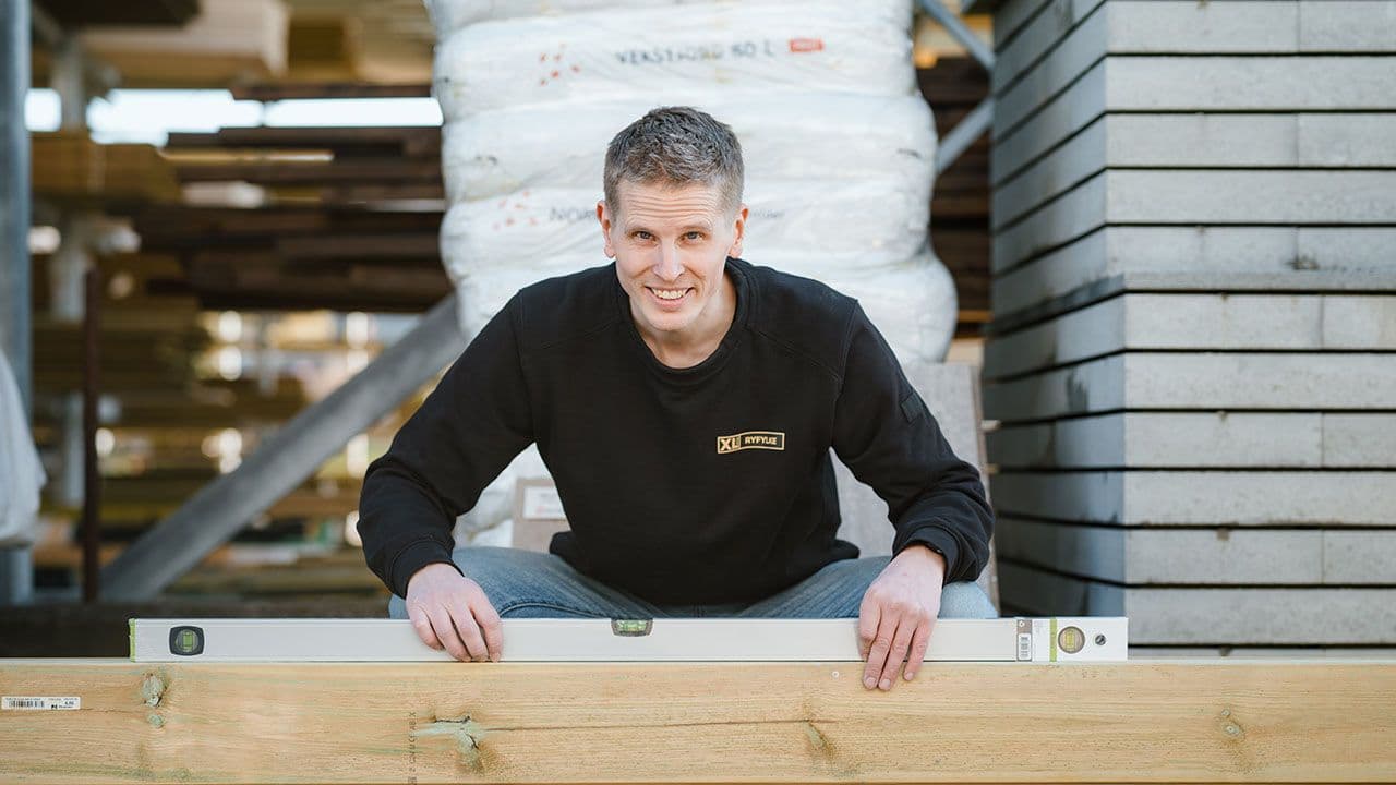 XL-BYGG ansatt som sitter på huk med vater på bjelkelag.