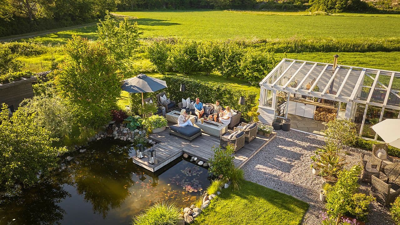 Et moderne uterom med royalimpregnerte terrassebord i stor hage med dam.