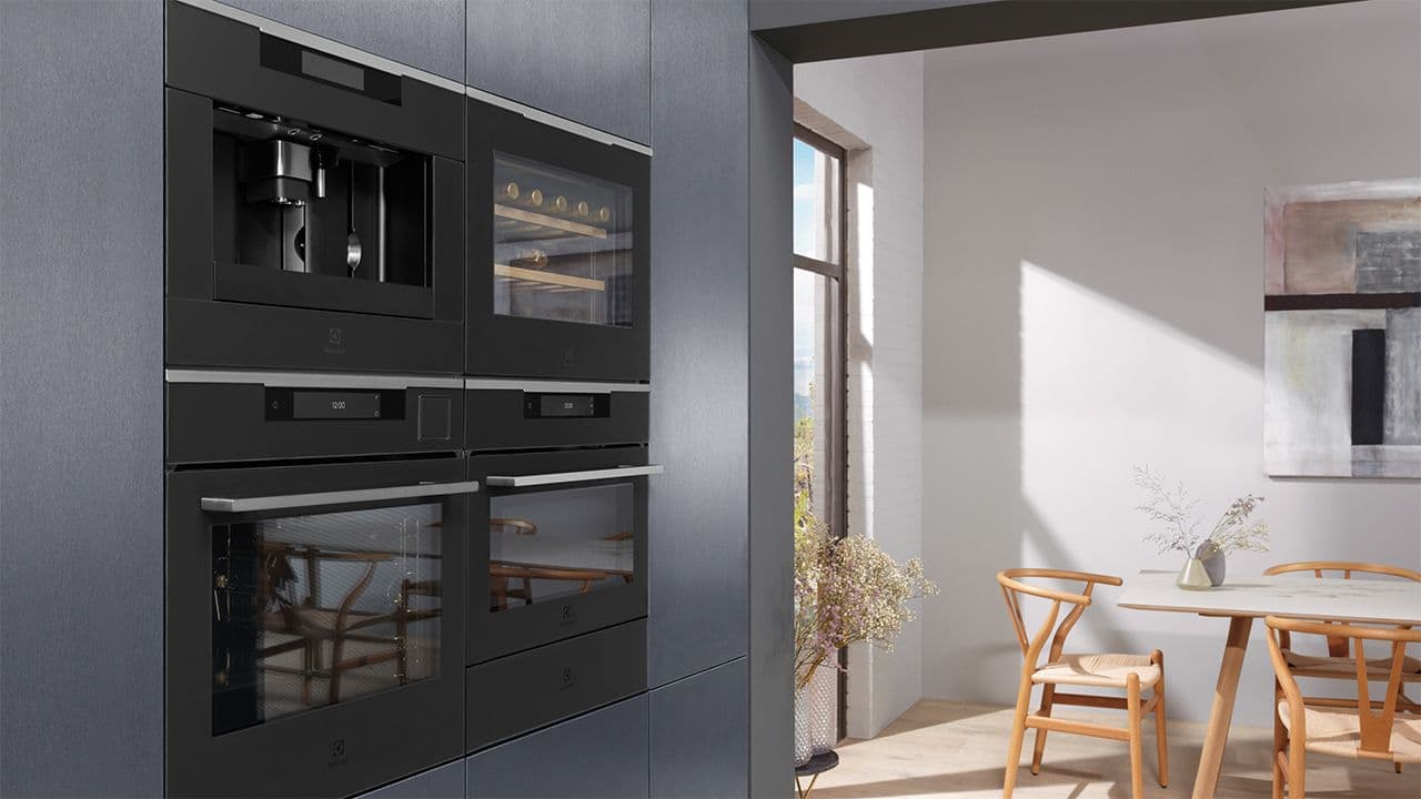 Hvitevarer i matt svart i høyskap på mørkt kjøkken.