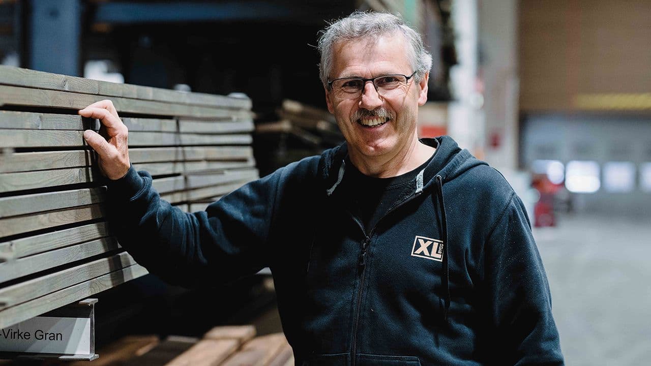 XL-BYGG ansatt som står og smiler og holder på en stabel med materiell.