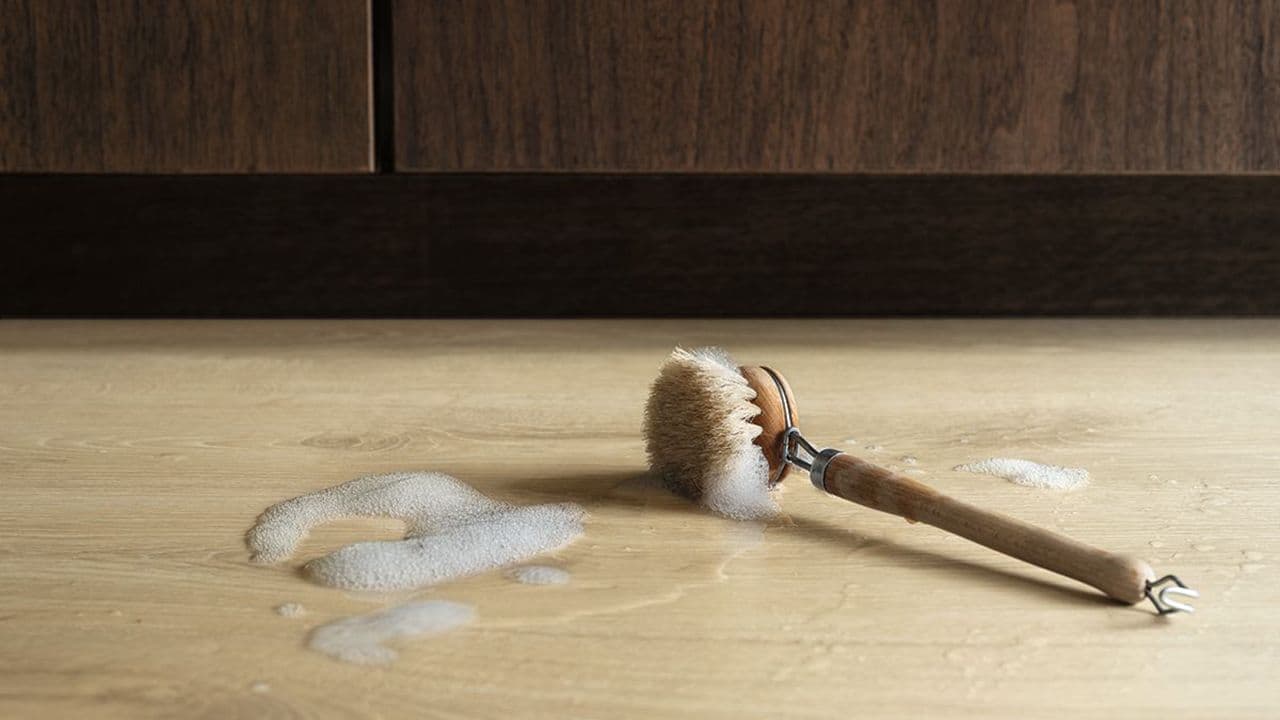 Oppvaskkost og såpevann som ligger på et laminatgulv.