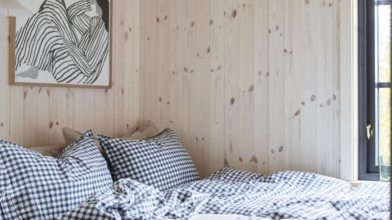 Hytte med lyse panelvegger på soverom med svarte vinduskarmer.