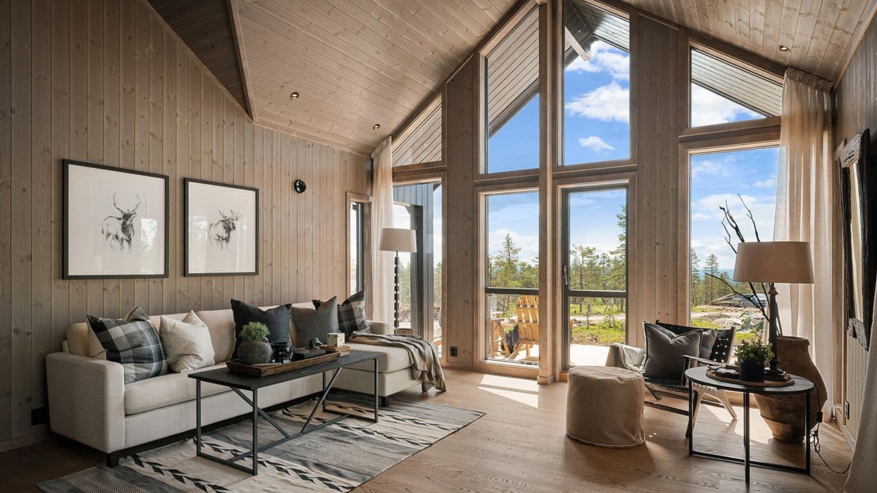 Moderne hytte med store vindusflater og lyst treverk.