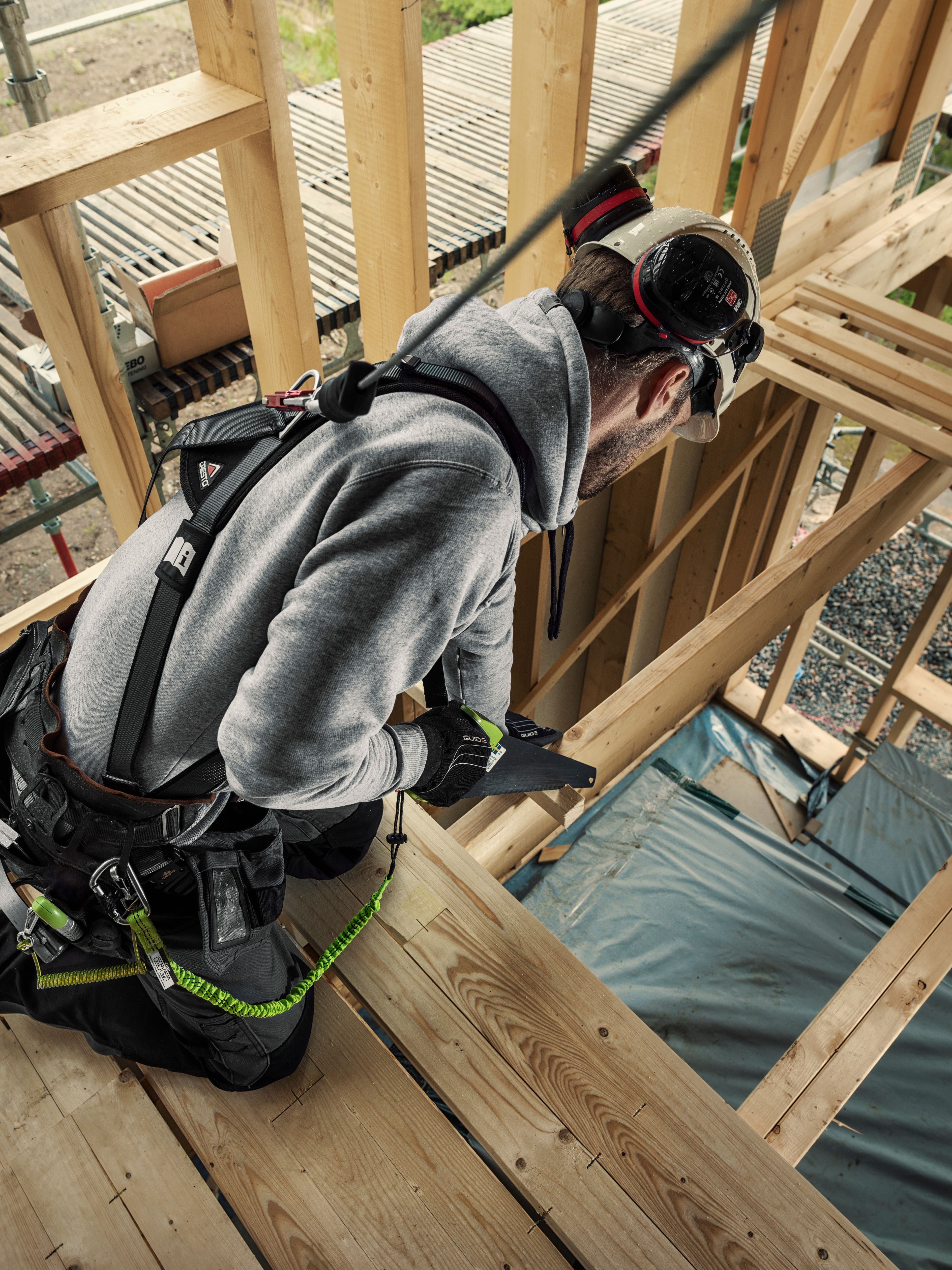 håndverker sager i høyden med verktøysikring på seg
