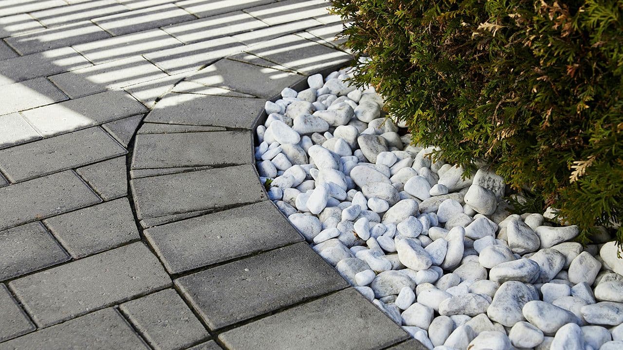Hvit dekorstein under hekken lagt ved siden av belegningsstein.