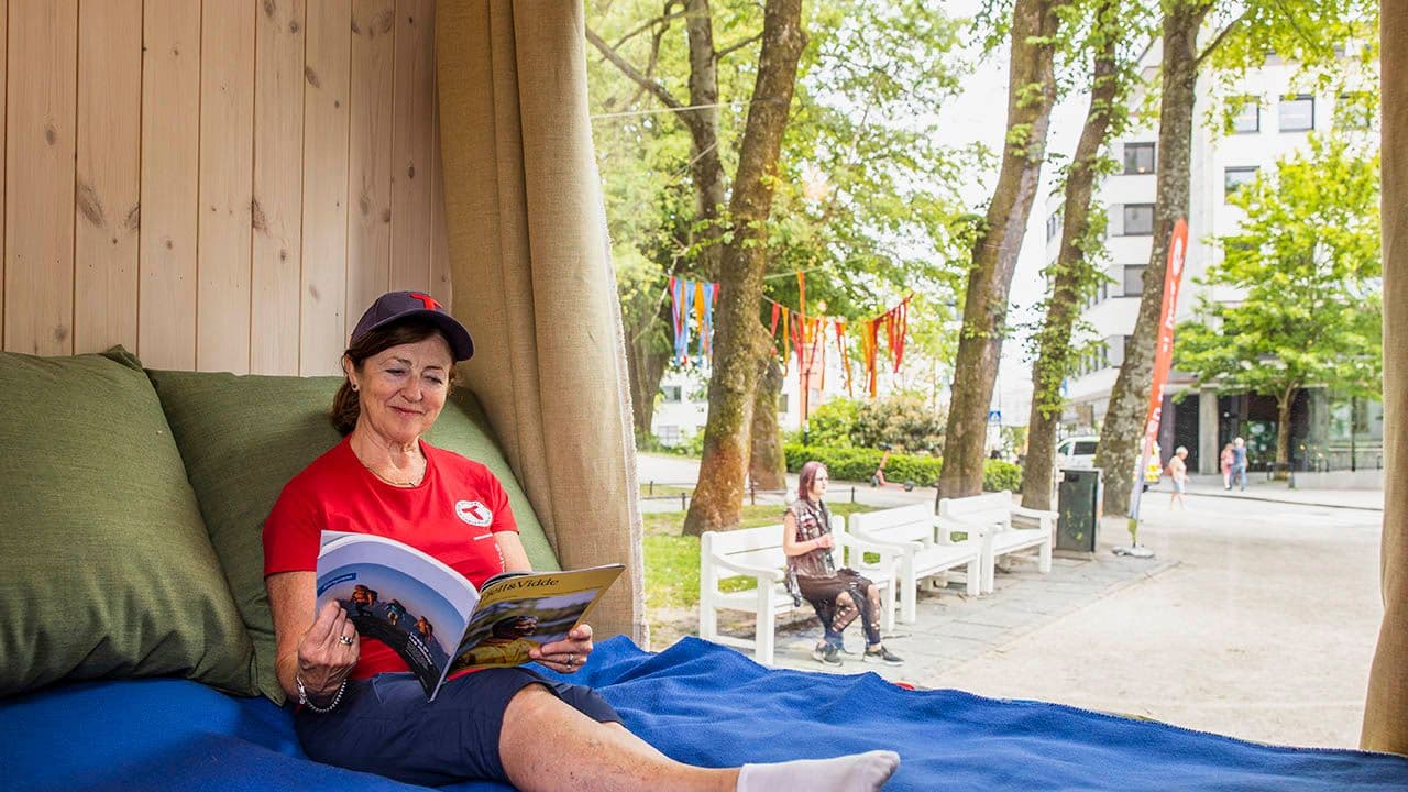 Person som sitter i dobbeltseng i minihytte med stort vindu bak.